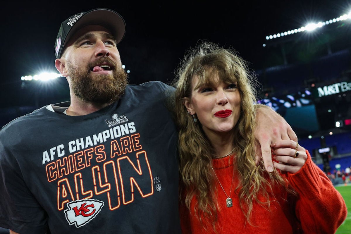 Travis Kelce and Taylor Swift look happy standing on a football field following a win by The Chiefs.