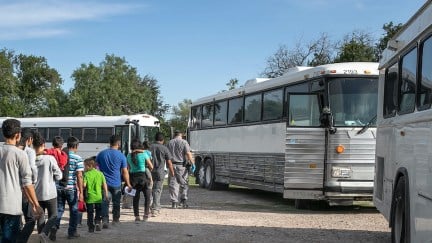 A line of migrants boards a large white bus.