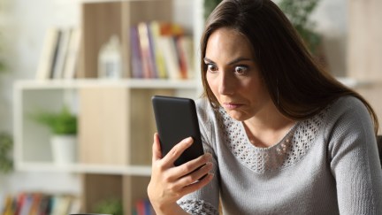 A woman looks at her cell phone with a comically exaggerated confused expression.