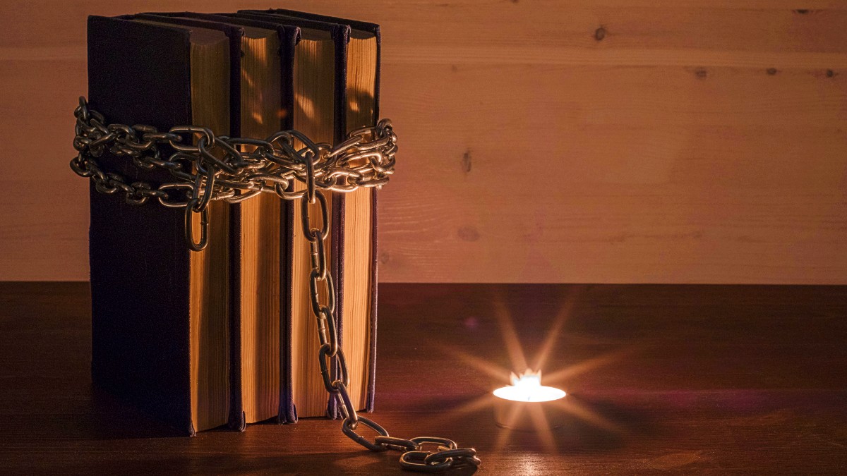 A stack of books in chains sits next to a candle