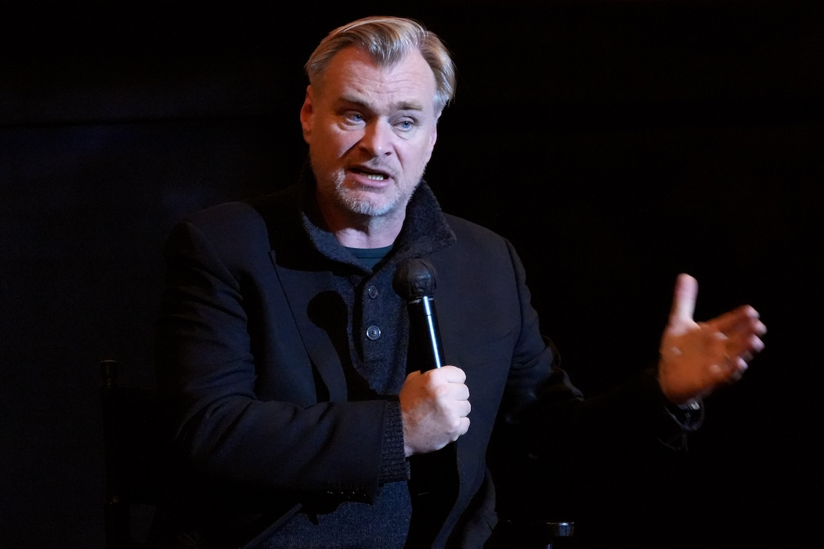Christopher Nolan sitting with a microphone and his hand out as he is talking