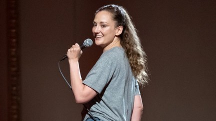 Comedian Jacqueline Novak speaks into a microphone and looks over her left shoulder in 