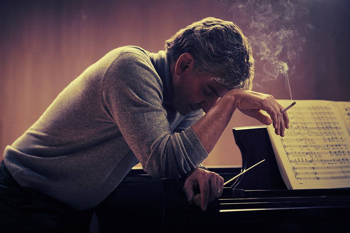 Bradley Cooper with his head in his hands leaning on a piano