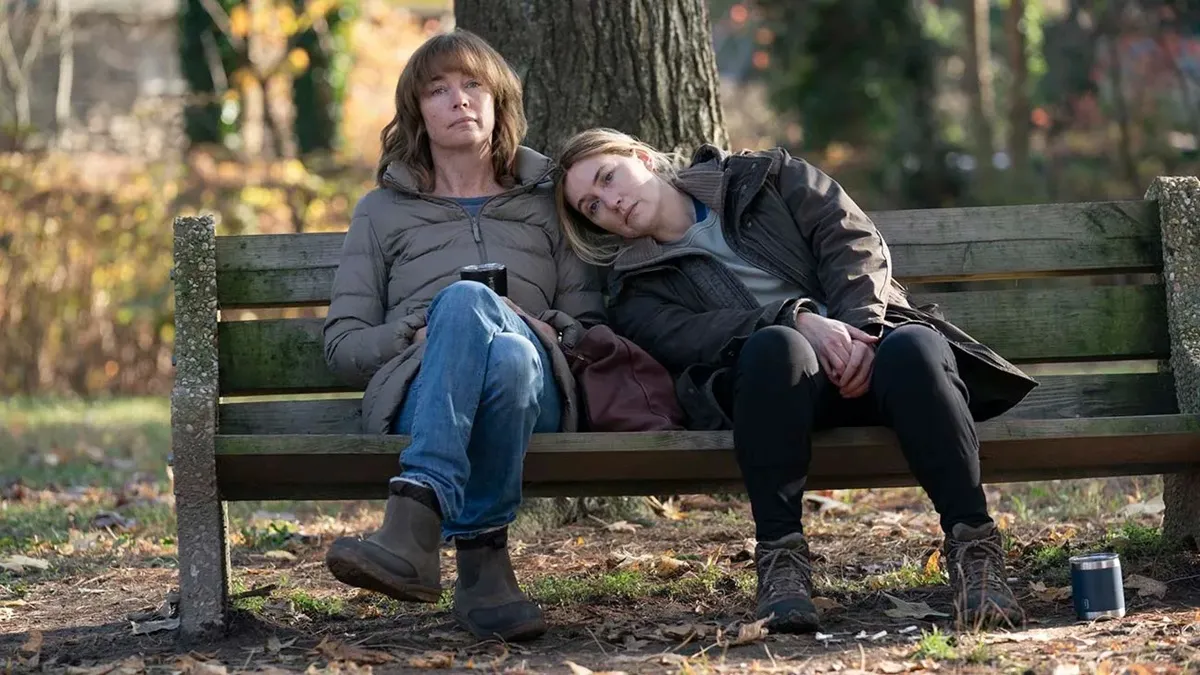 two women sit on a bench, one woman with her head on the other's shoulder