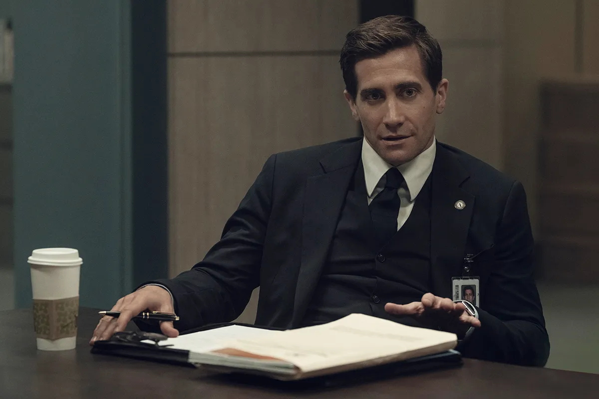 Jake Gyllenhaal as Rusty, sitting at a table with papers in front of him