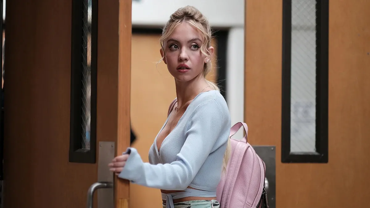 Sydney Sweeney dressed as a teenager pausing in a school doorway in Euphoria