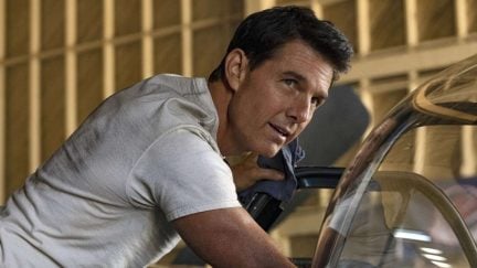 Tom Cruise wears a white t-shirt and leans over a car in Top Gun Maverick