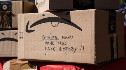An Amazon package in a warehouse with a message written on the side in Sharpie: 