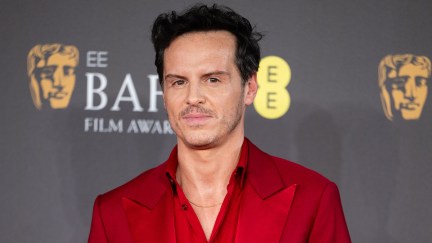 Andrew Scott in a red tuxedo gives a stern smile on the BAFTAs red carpet.