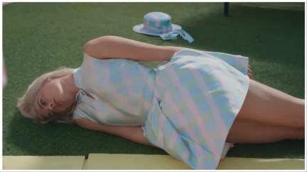 Barbie (Margot Robbie) lies down on the ground on her side in defeat in 'Barbie'.