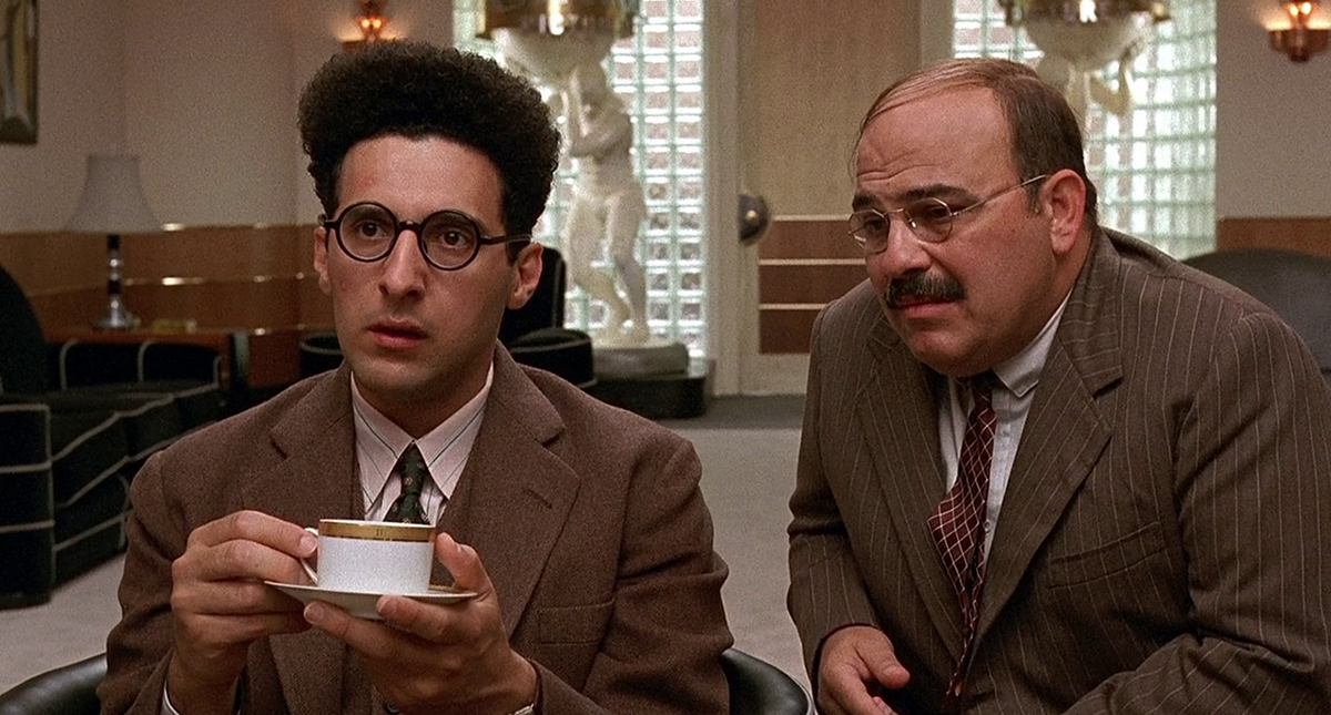 Barton Fink sitting with a mug next to a man