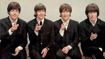 Paul McCartney, Ringo Starr, John Lennon and George Harrison pose for a photo smiling and all pointing at the camera
