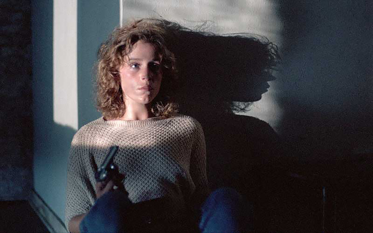 Frances McDormand sitting against a wall with a gun in her hand