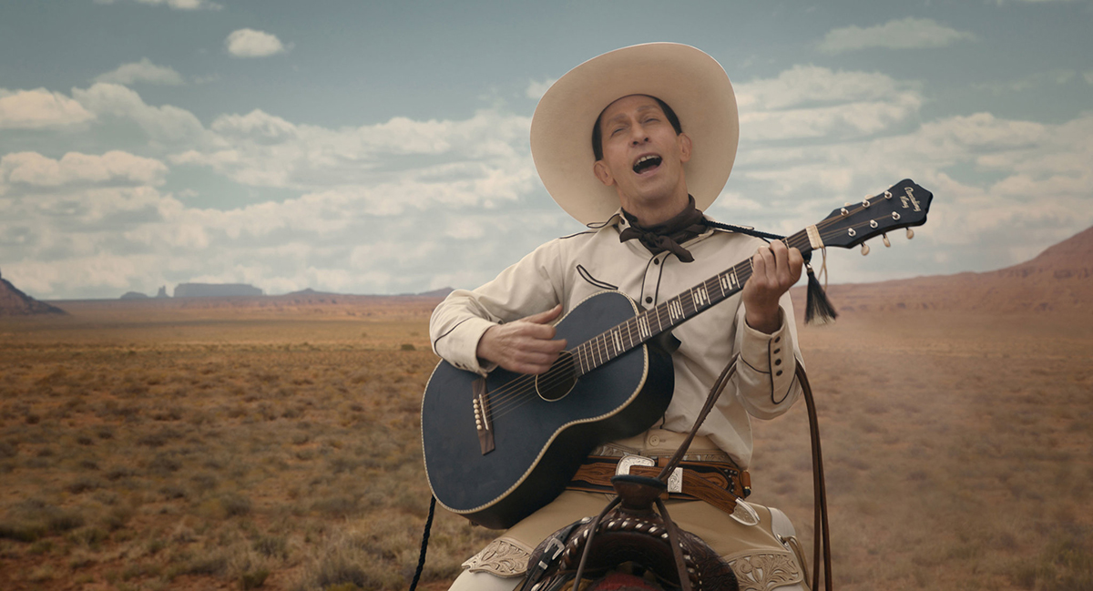 Tim Blake Nelson on a horse playing a guitar dressed like a cowboy