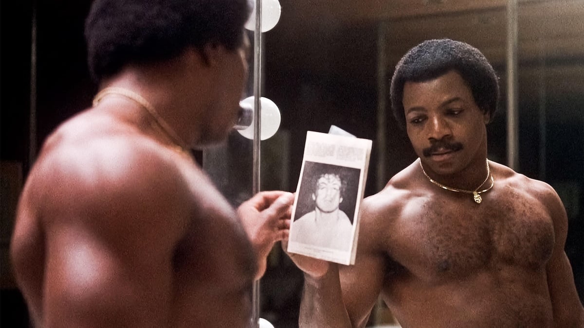 Carl Weathers as Apollo Creed looking in a mirror at a picture of Rocky Balboa
