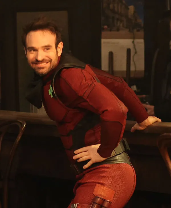 Charlie Cox bends over in his Daredevil suit, looking over his shoulder and grinning.