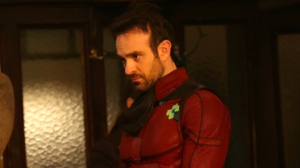 Charlie Cox frowns at something off camera, wearing his Daredevil suit.