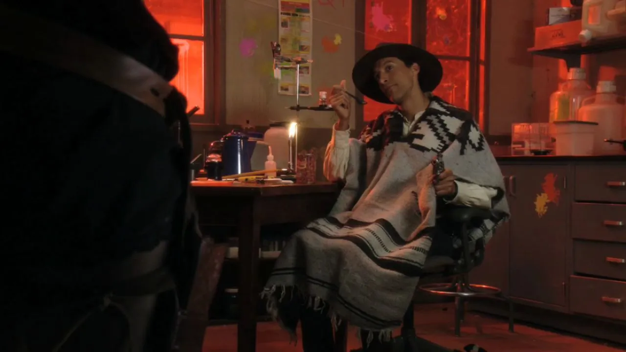Sitll from Community episode A Fist Full of Paintballs; Danny Pudi, wearing a black cowboy hat and grey poncho, sits at a lab table eating beans from a can.