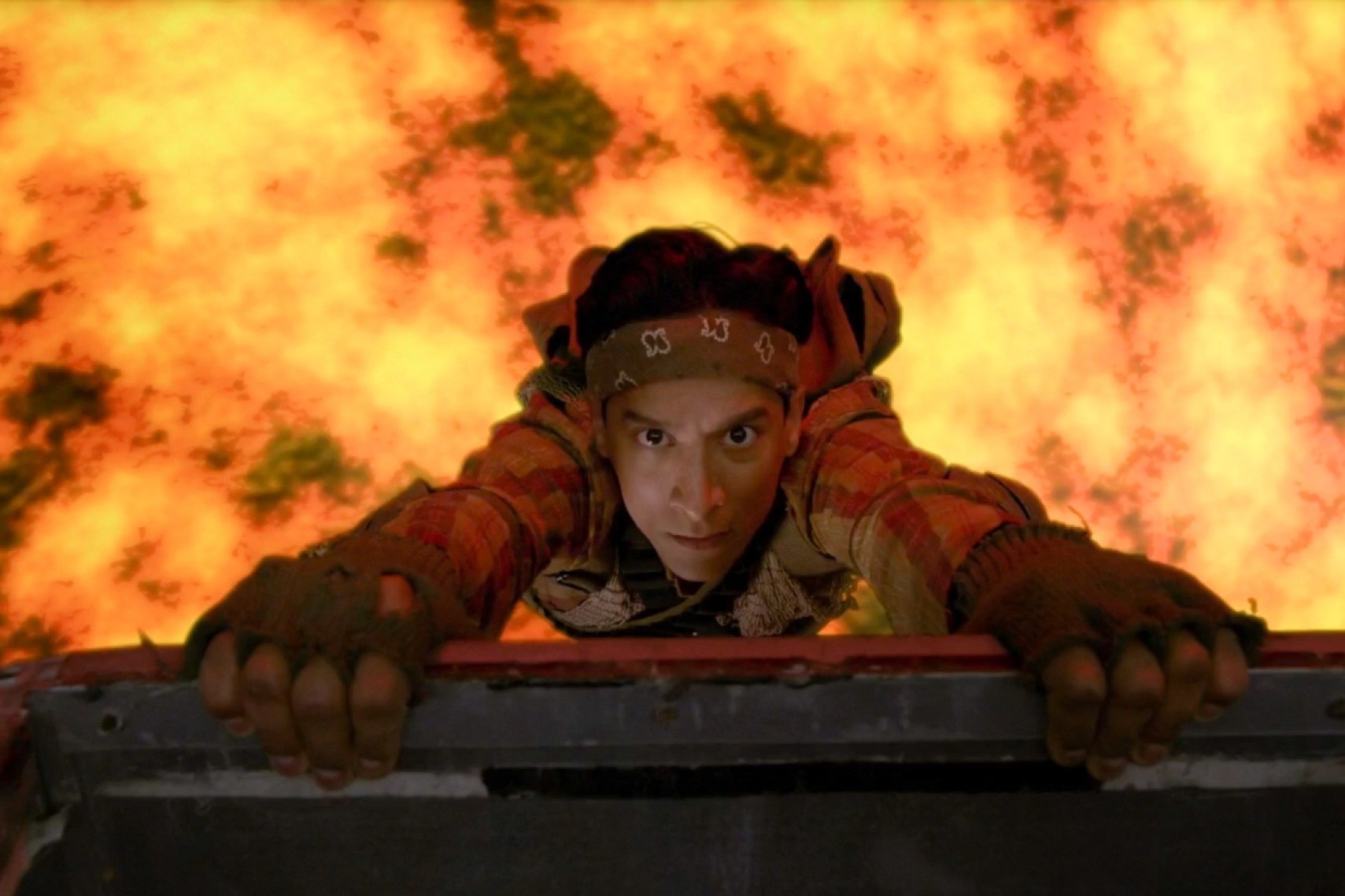 Still from Community episode Geothermal Escapism; Danny Pudi,  wearing army gear, dangles over lava.
