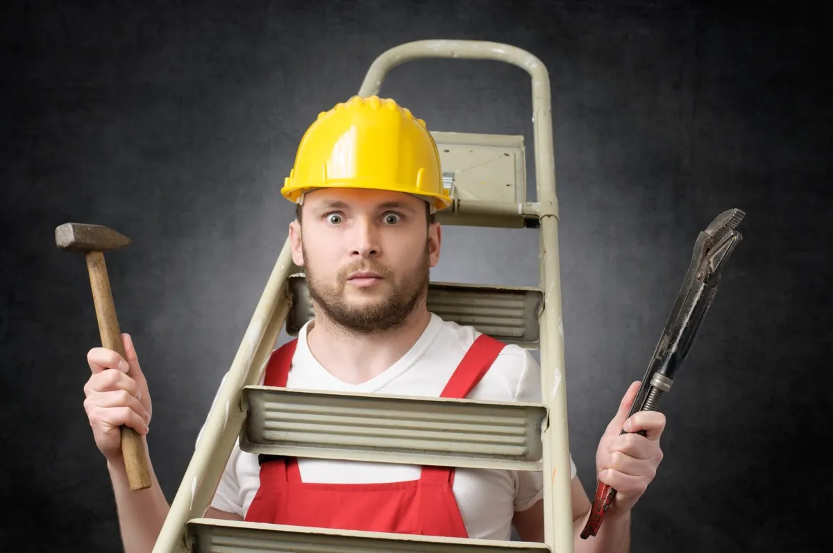 Clumsy worker with ladder, hammer and pipe wrench