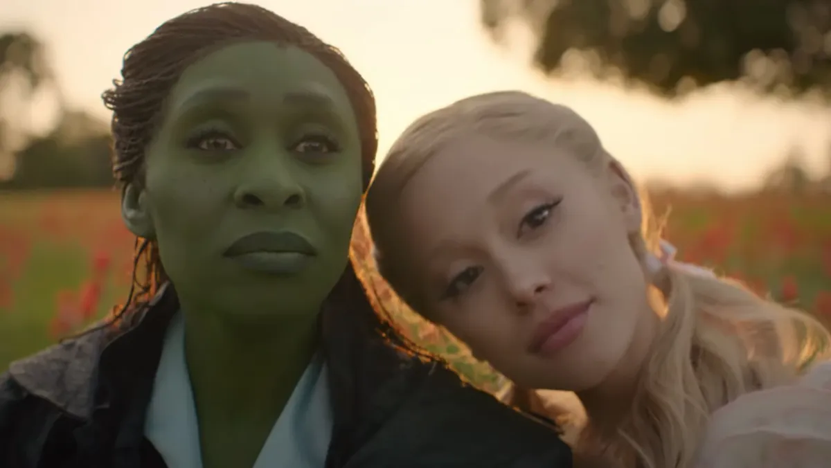 Glinda leaning her head on Elphaba's shoulder as they sit in a field