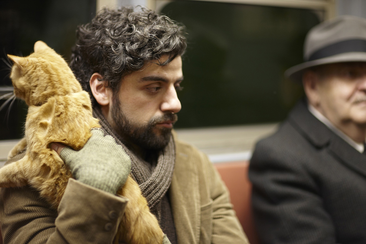 Oscar Isaac holding a cat on a subway wearing gloves