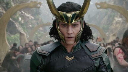 Loki wears his horns in Thor: Ragnarok, with other characters battling behind him.