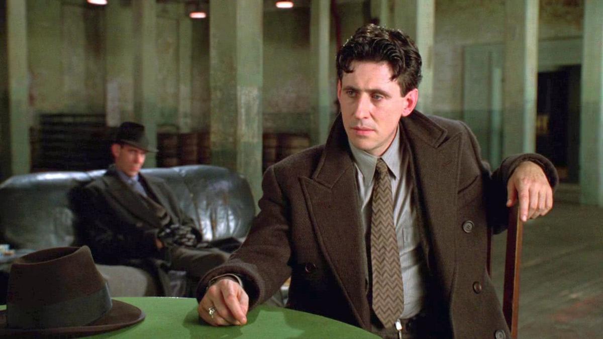 Gabriel Byrne sitting at a table in a suit in Miller's Crossing