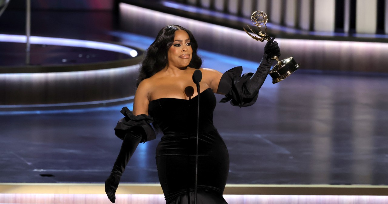 Niecy Nash stands on stage at the Emmys holding her trophy up high.