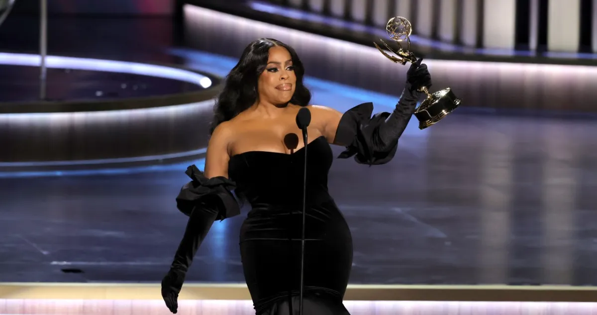 Niecy Nash stands on stage at the Emmys holding her trophy up high.