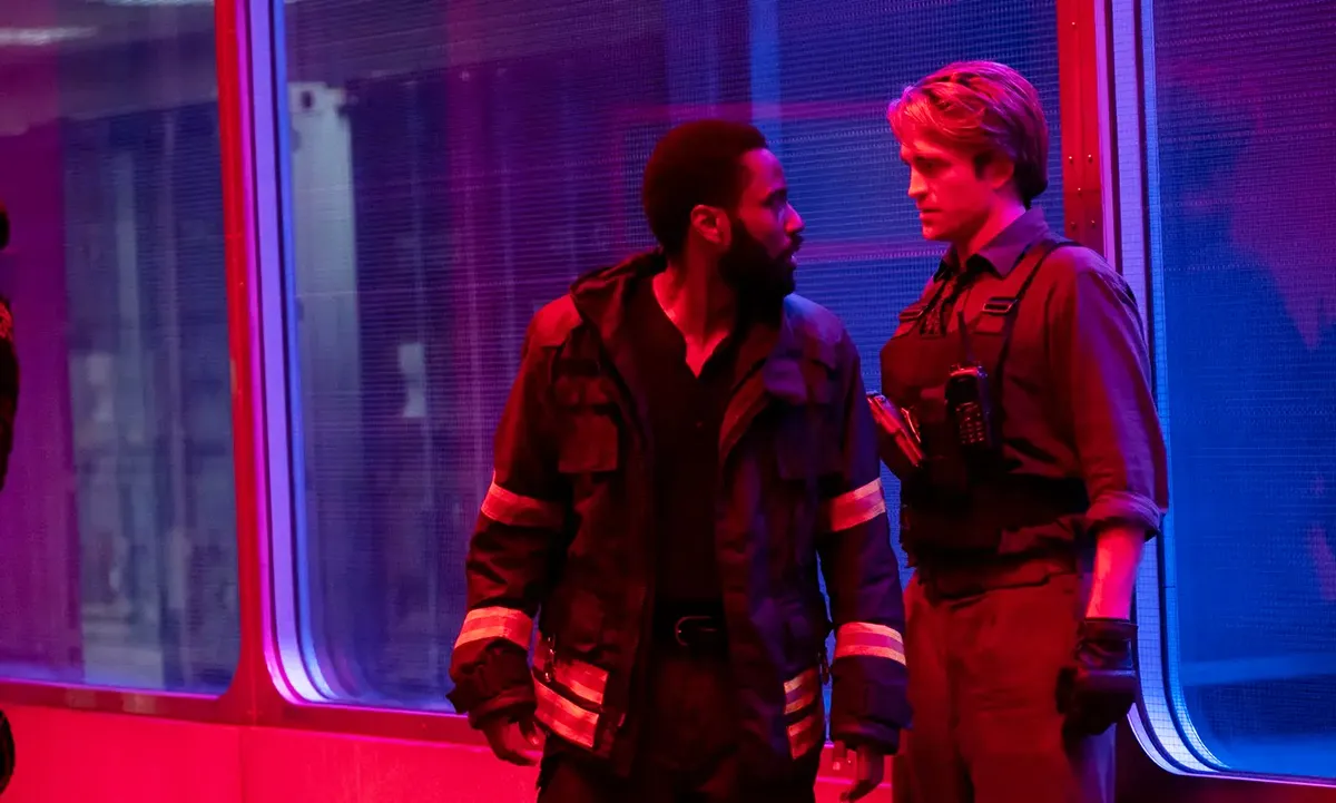 Robert Pattinson and John David Washington standing together in blue and red lighting