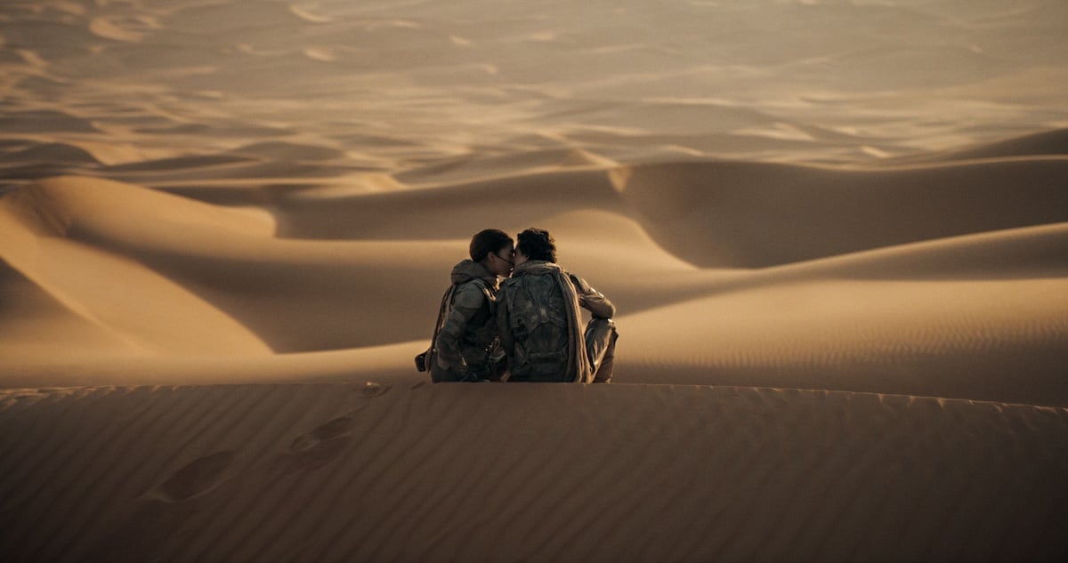 Chanti (Zendaya) and Paul (Timothée Chalamet) sitting on Arrakis and kissing