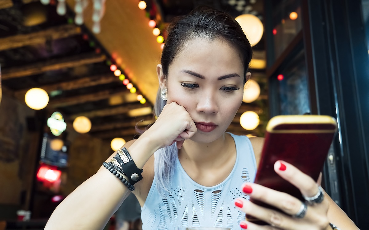 A woman stares at her phone, looking displeased.
