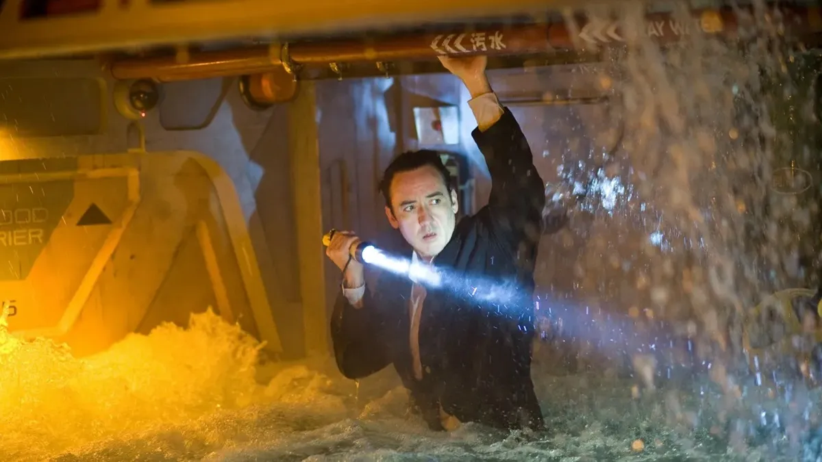 John Cusack holds a flashlight as he wades through a flooded ship