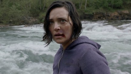 A woman with a bloodied lip stands in front of a raging river