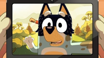 Bandit waves from the screen of a tablet, covered in dirt with a natural landscape behind him.