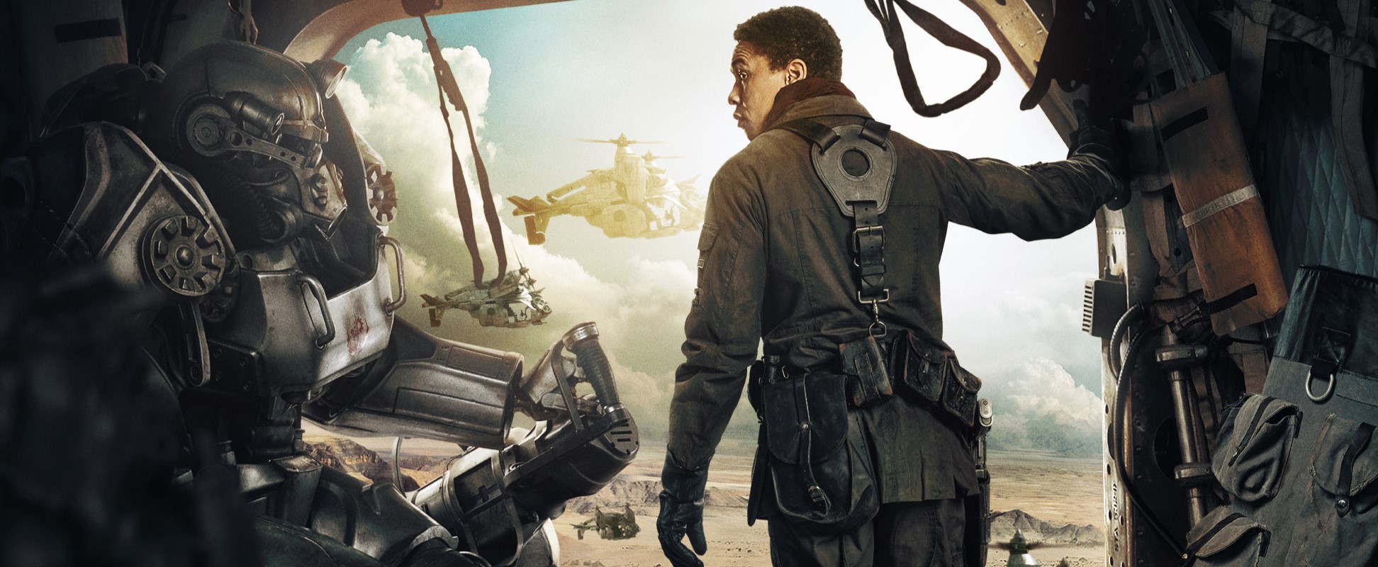 Cropped promotional image of Aaron Moten as Maximus in 'Fallout.' Maximus is a young Black man with short hair wearing a Brotherhood of Steel uniform and standing in the open side of a flying vertibird. He is looking over his shoulder at someone in power armor who's sitting in the cabin with him. 