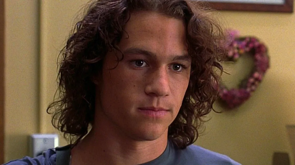 Image of Heath Ledger as Patrick in '10 Things I Hate About You.' Patrick is a white teenage boy with chin-length, wavy brown hair. He's wearing a blue t-shirt and staring soulfully off camera.
