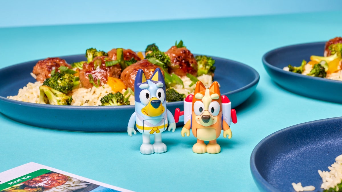 Plastic Bluey and Bingo action figures surrounded by plates of food.