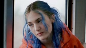 Image of Kate Winslet as Clementine in 'Eternal Sunshine of the Spotless Mind.' She is a white woman with dyed blue hair with light brown roots showing worn half up and half down. She's wearing a bright orange hoodie.