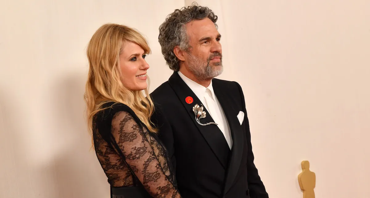 Mark Ruffalo and Sunrise Coigney pose for a photo at the Oscars. Ruffalo is wearing a red circular enamel pin on his lapel.