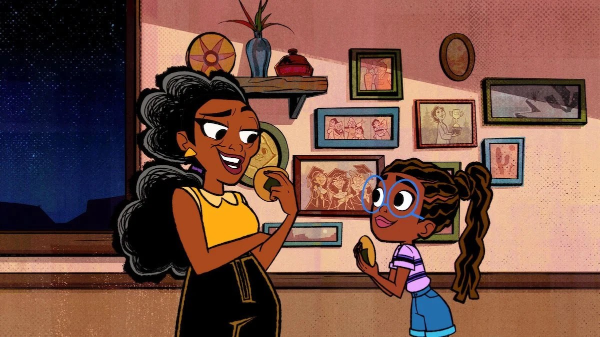 A Black girl and her grandmother standing in a hallway having a conversation, and there are family pictures on the wall behind them. 