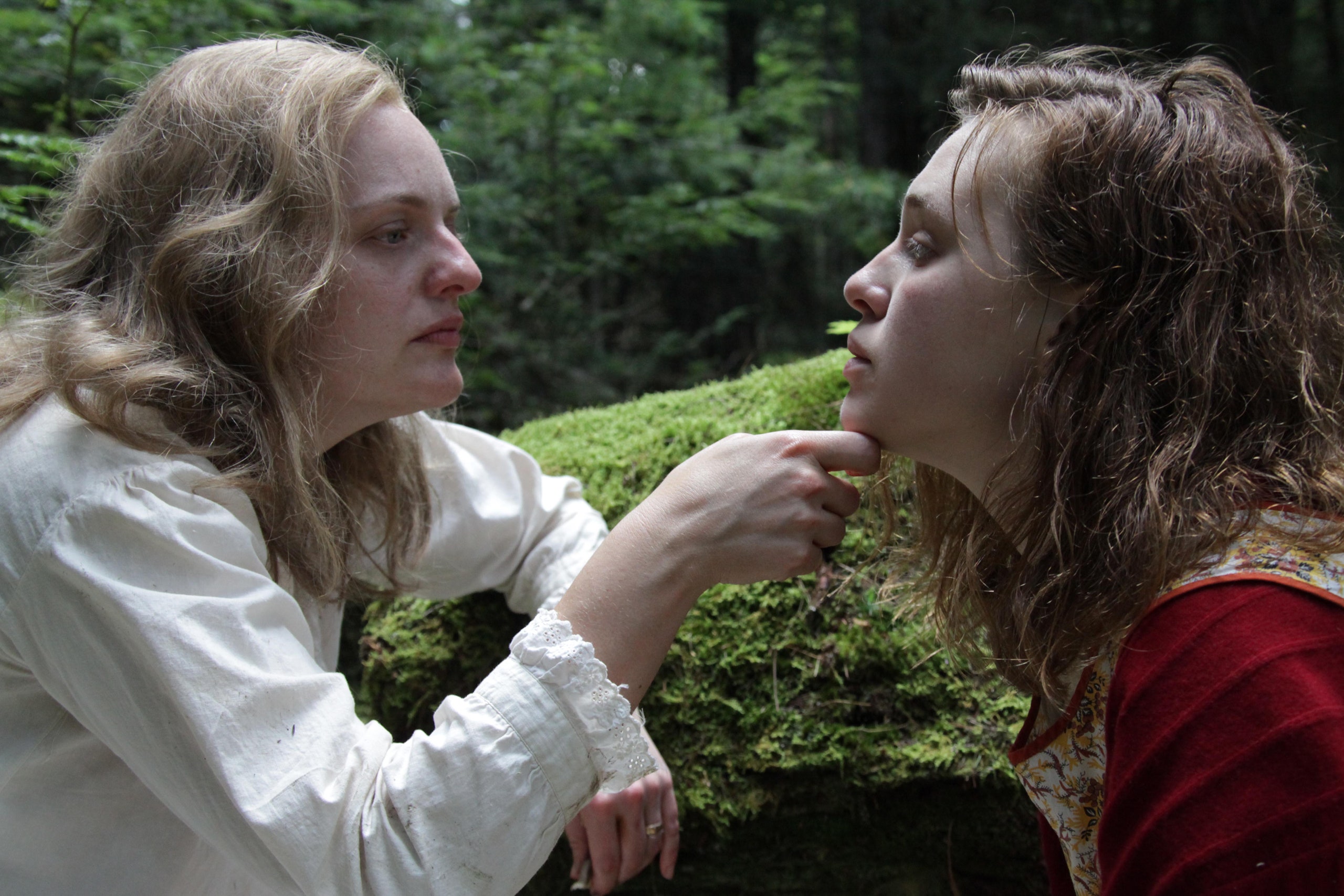 two women in the woods, one woman is holding the second woman's chin