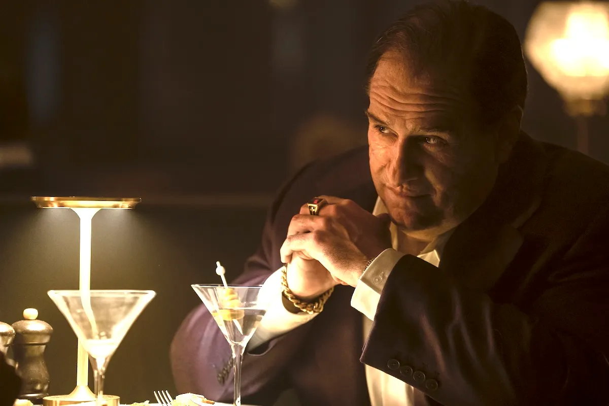Colin Farrell as the Penguin sitting at table with a martini glass