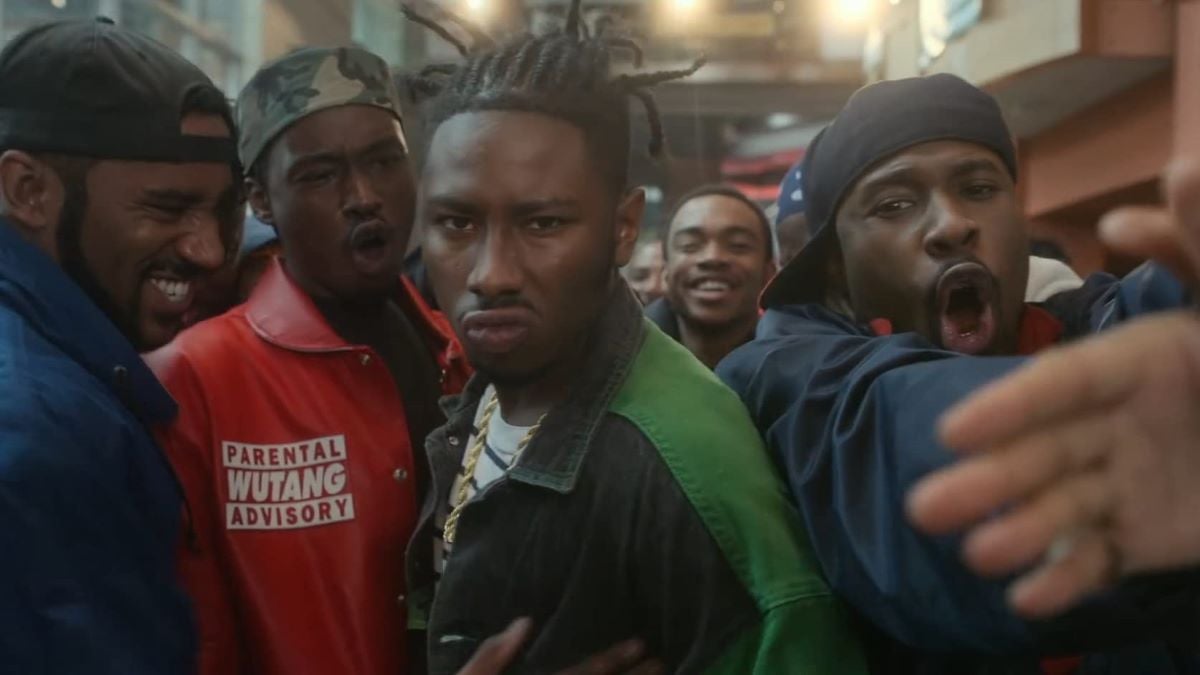 Image of the cast of 'Wu-Tang: An American Saga.' Three young black men  are in the middle of a crowd. The one in the center is mean-mugging for the camera, the others are cheering and smiling. 