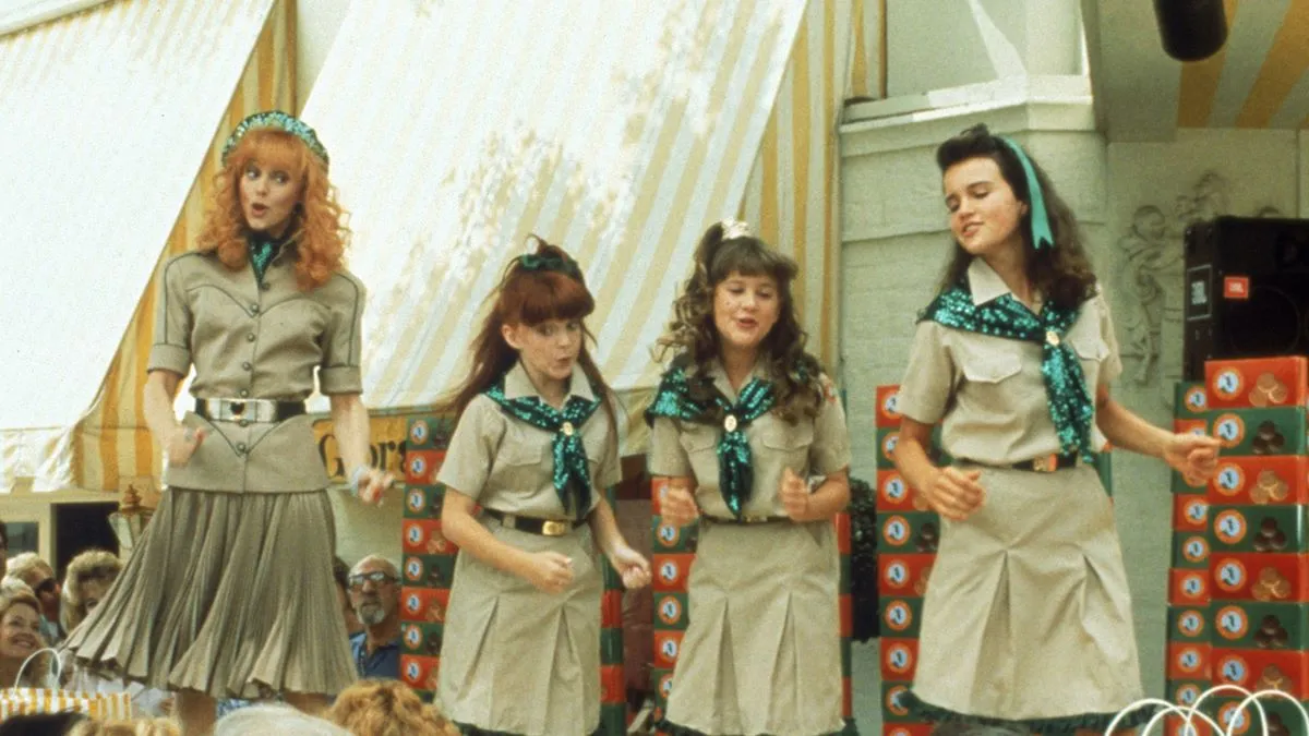 Image of Shelley Long as Phyllis, Emily Schulman as Tiffany, Kellie Martin as Emily, and Carla Guigino as Chica in 'Troop Beverly Hills.' They are mid song performance and wearing their customized Wilderness Girl uniforms. 
