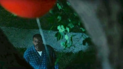 A Black man gazes up worriedly at a red balloon at night.