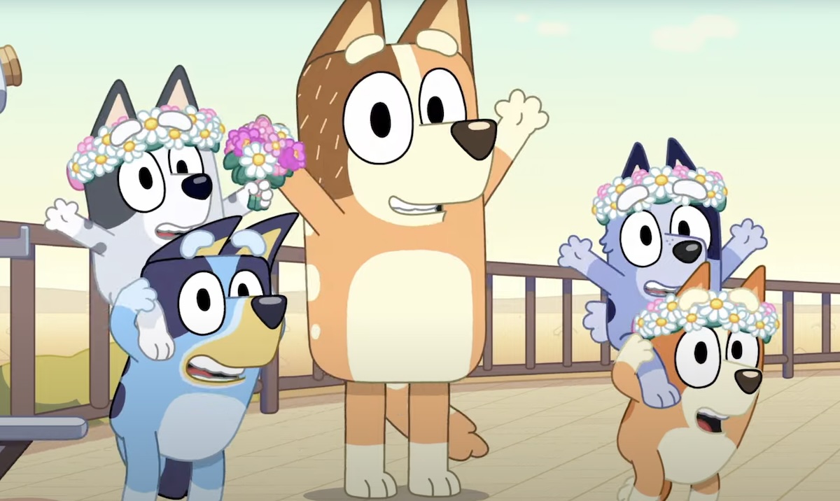 Bluey, Muffin, Socks, Bingo, and Chilli all smile and hold their arms up. The kids are wearing flower crowns.