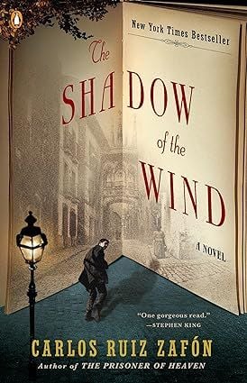 Cover of Carloz Ruiz Zafon's The Shadow of the Wind; a illustration of a man walks into a pencil drawing of a landscape on the pages of an open book. A lampost is behind him.