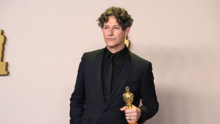Jonathan Glazer holds an Oscar award against a plain background.
